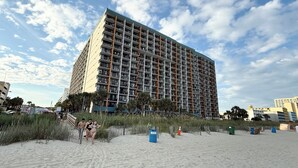 Een hoog hotel met meerdere balkons, nabij een zandstrand.