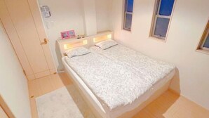 A single bed with a white duvet, a bedside table with a lamp, and a window with a view of the sky. - Xiao Ban Yaju (Osaka)