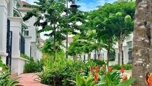 A pathway flanked by lush greenery and flowering plants, leading to a white building with a red roof. - Sunrise Villa (Phu Quoc Island)