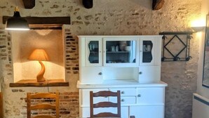 A rustic kitchen with exposed brick walls, wooden beams, a white cabinet with glass doors, and a table with chairs. - Gîtes du Martroy (Nargis)
