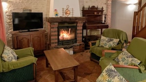 A cozy living room with a fireplace, wooden furniture, and a television. - Gîtes du Martroy (Nargis)