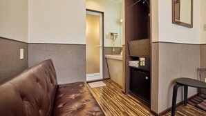 A compact room with a brown leather sofa, a small table, a wardrobe, and a mirror on the wall. - HOTEL GRAND FORT (Tokyo)