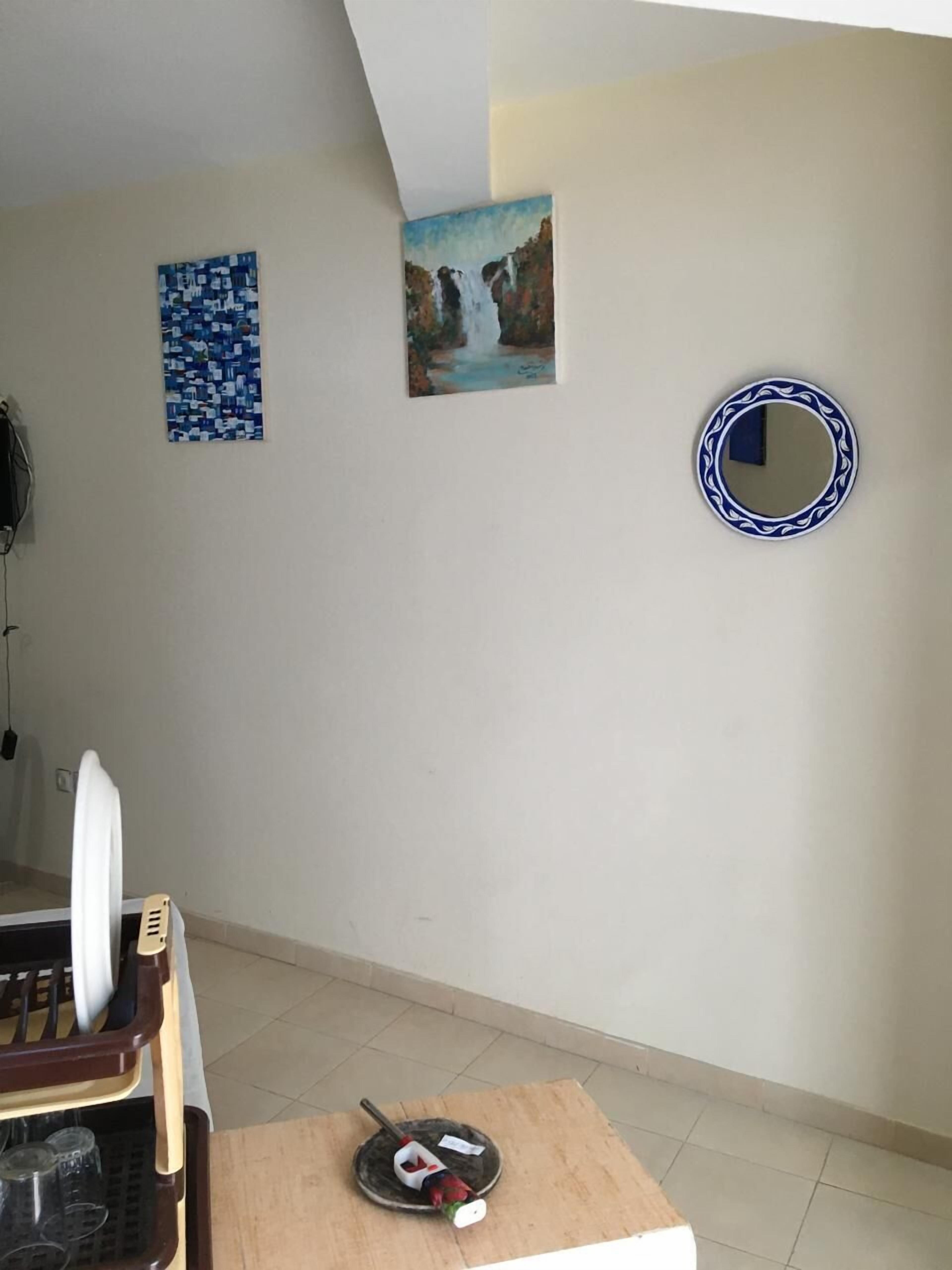 Una habitación con una mesa de comedor, una silla, una pequeña mesa con una botella y un vaso, y dos cuadros colgados en la pared.