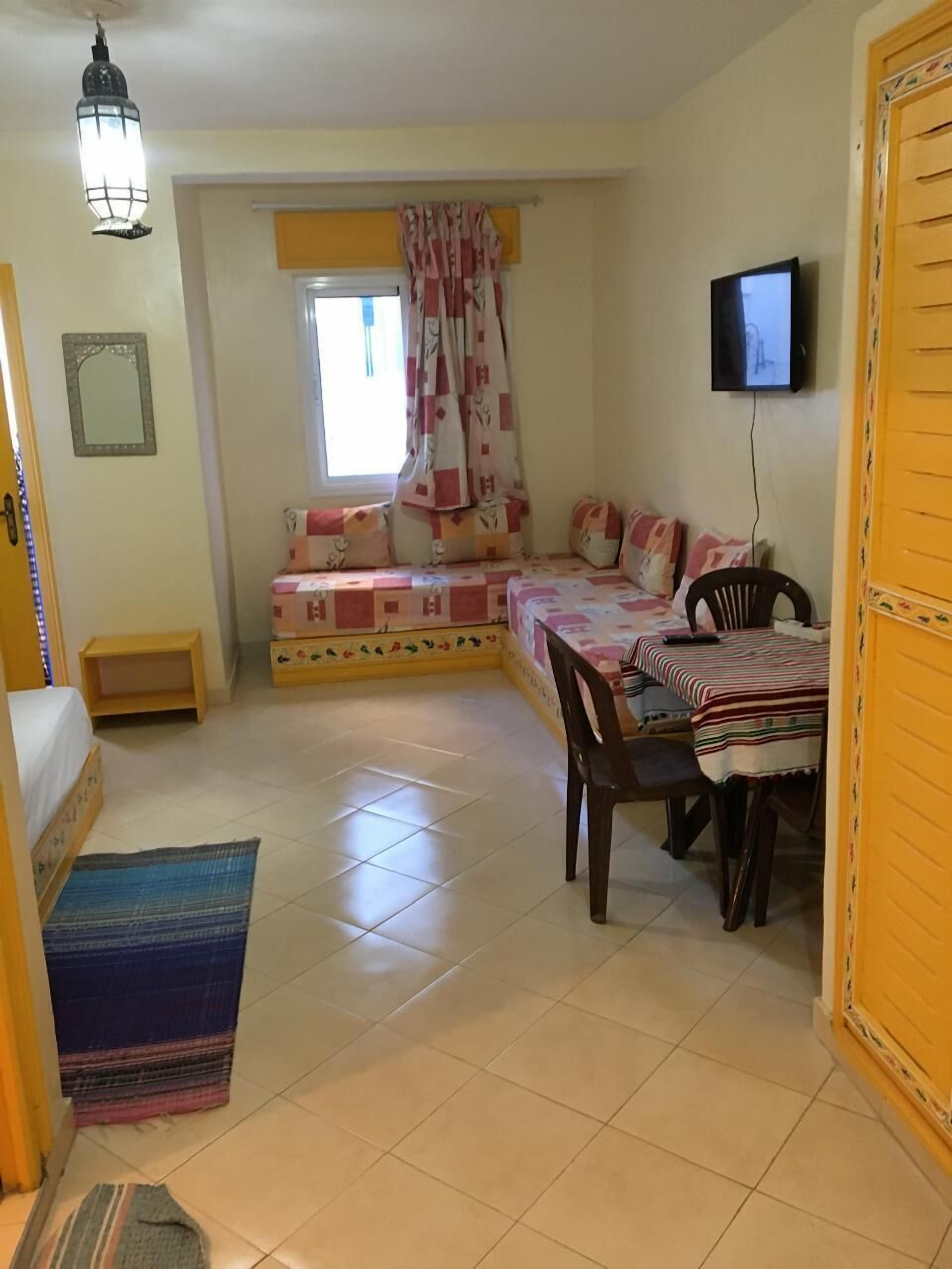 A cozy room with a bed, a small table, a chair, a TV, and a window with curtains.