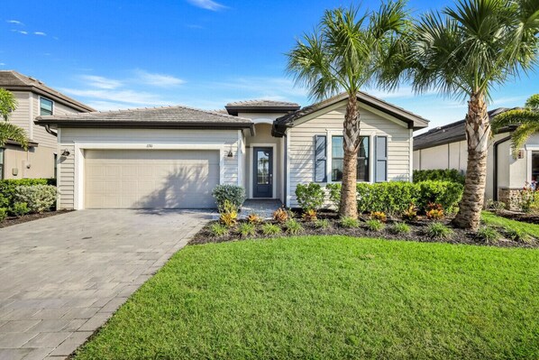 A two-story house with a garage, a well-maintained lawn, and a variety of plants and shrubs.