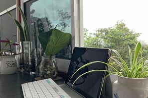 Ein Laptop auf einem Schreibtisch mit Blick aus dem Fenster, einer Tastatur und Topfpflanzen.