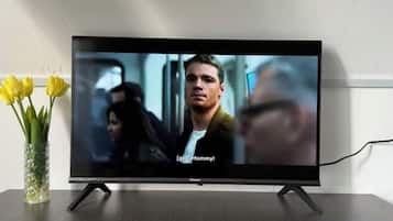 A flat-screen TV on a stand with a vase of yellow flowers to the left.