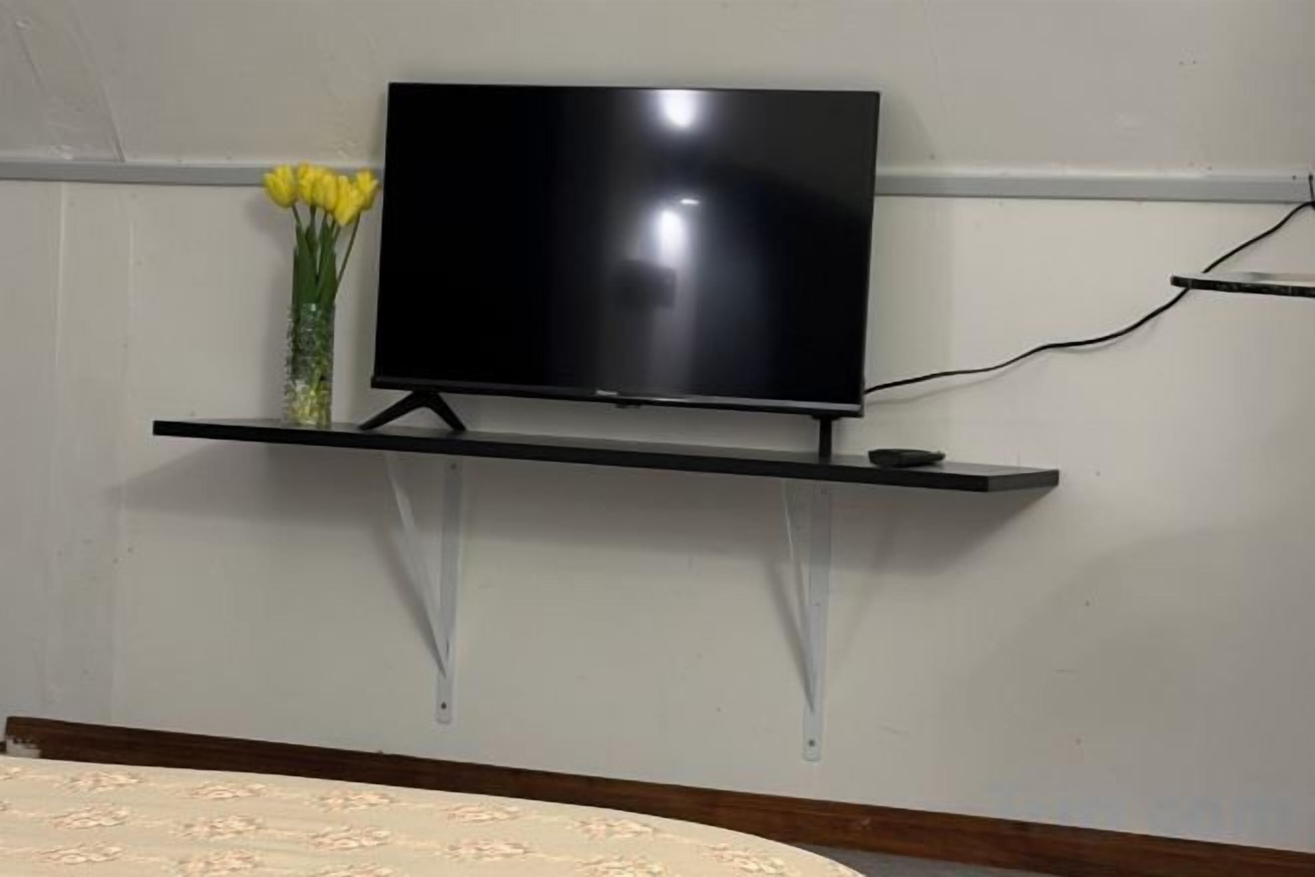 A television mounted on a wall with a flower arrangement beside it.
