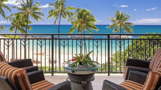 Un balcone con mobili in vimini, un tavolino in vetro con una pianta e vista sulla spiaggia e sull'oceano.