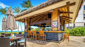 Un bar sulla spiaggia con mobili in legno e tetto di paglia.