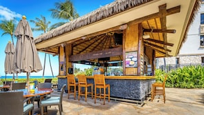 Un bar situé en bord de mer, avec des meubles en bois et un toit de chaume.