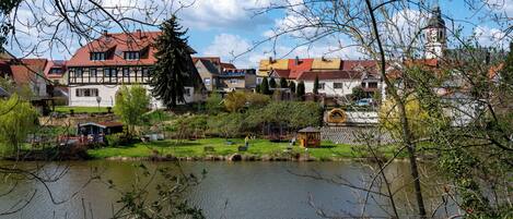 A riverside view of a town with traditional buildings, a clock tower, and a gazebo by the water.