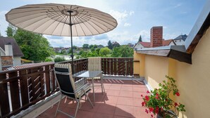 A balcony with a table and chairs, a potted plant, and a large umbrella. - Boardinghouse - temporary living (Frohburg)