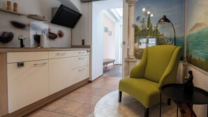 A modern kitchen with white cabinets, a flat-screen TV, and a dining area with a green armchair and a small table. - Boardinghouse - temporary living (Frohburg)