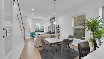 A modern living room with a dining area, a staircase, and a large window with a brick wall.