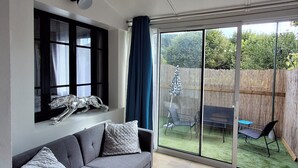 A modern living room with a grey sofa, a small round table, and a large sliding glass door leading to a backyard. - La Discrète Romantique, apartment with jacuzzi (Charavines)