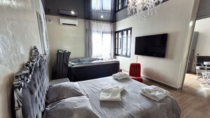 A modern bedroom with a large bed, a flat-screen TV, a chandelier, and a view of the outdoors. - La Discrète Romantique, apartment with jacuzzi (Charavines)