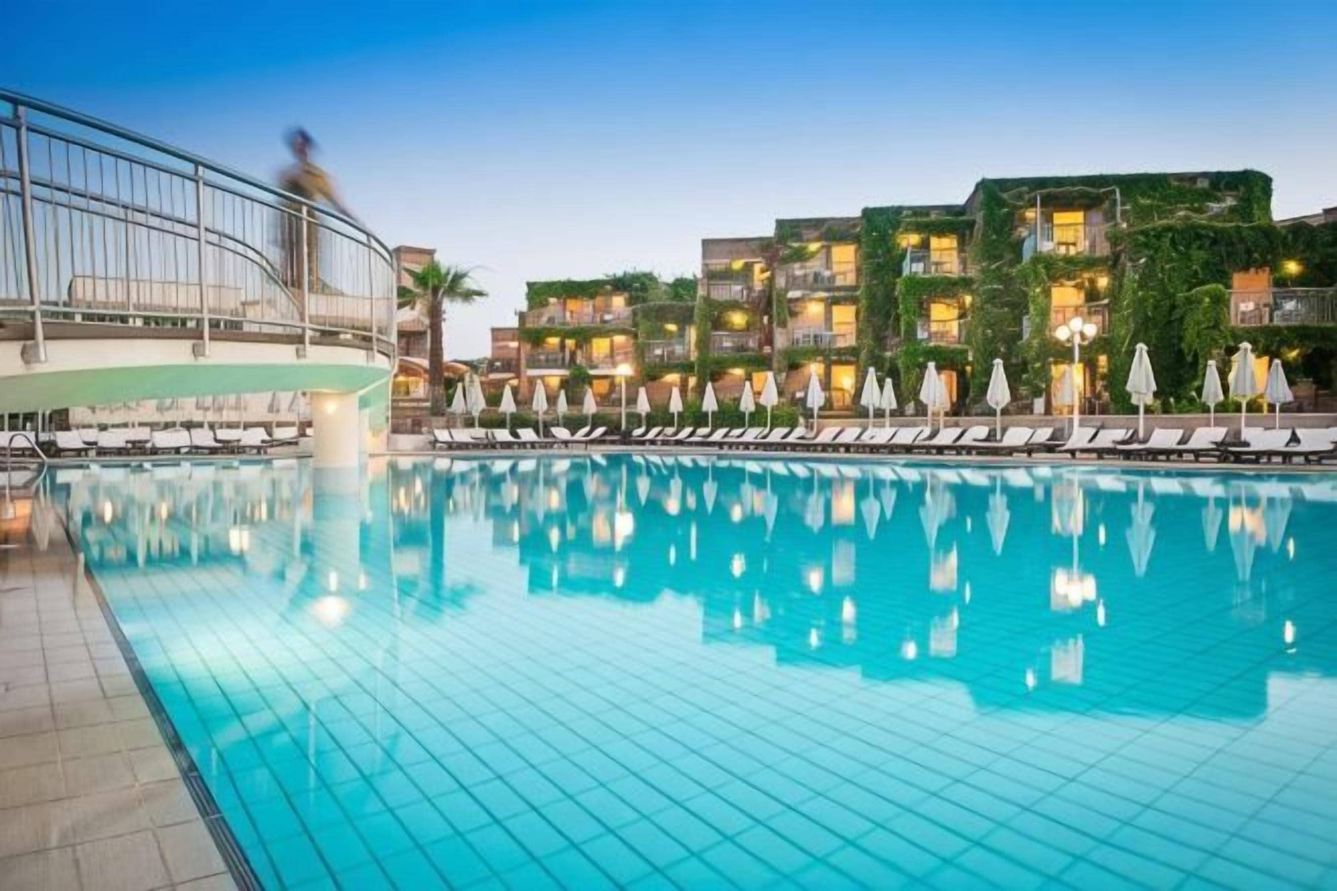 A swimming pool with lounge chairs and umbrellas, surrounded by multi-story buildings with balconies.