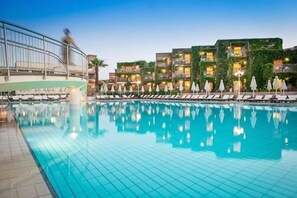 A swimming pool with lounge chairs, a building with balconies, and a person walking by. - Bella Beach Hotel (Agkisaras)