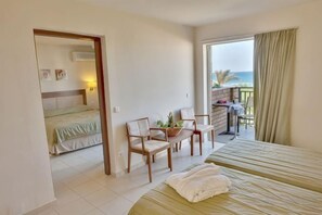 A hotel room with a bed, a desk, chairs, a balcony with a view of the sea, and a separate bedroom with a bed. - Bella Beach Hotel (Agkisaras)