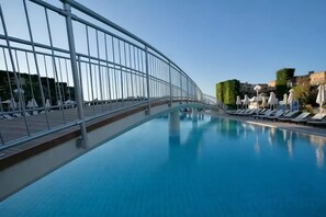 A pool area with a glass balustrade, lounge chairs, and umbrellas. - Bella Beach Hotel (Agkisaras)