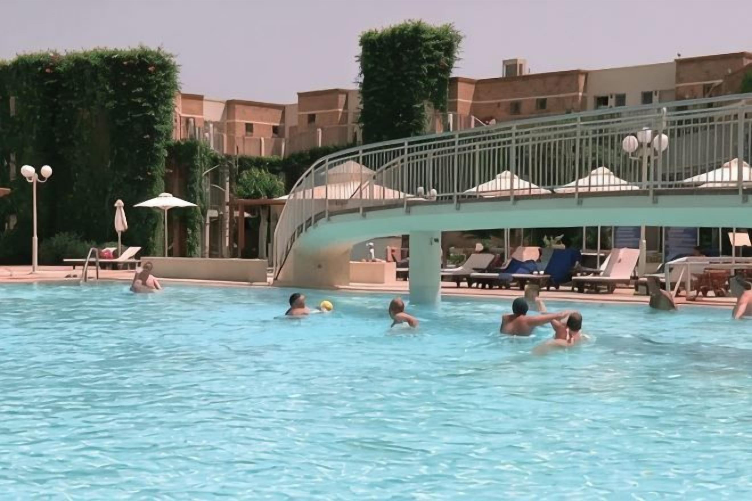 Piscina com pessoas, espreguiçadeiras e uma ponte.