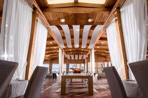 Un vaste espace intérieur avec des poutres en bois, une table centrale et des chaises disposées pour les repas.