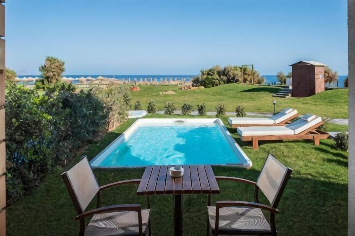 A swimming pool with lounge chairs and a table, surrounded by greenery and a view of the ocean.