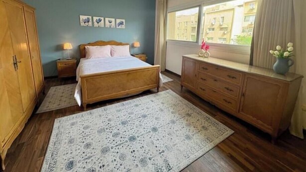 Un dormitorio con cama, armario de madera, cómoda y ventana con vistas a edificios.