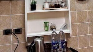 A kitchen with a white shelf unit holding kitchen utensils, a kettle, and water bottles. - Vintage Charm: 3BR, 2 baths in the heart of Zayed (Sheikh Zayed)