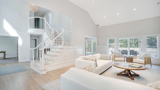A spacious living room with a white staircase, a large window, and a cozy seating area.