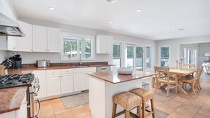 A modern kitchen with white cabinets, granite countertops, a central island, and a dining area with wooden chairs and a table.