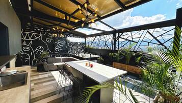 A modern outdoor dining area with a geometric metal roof, a concrete bar, and a wall with abstract art.
