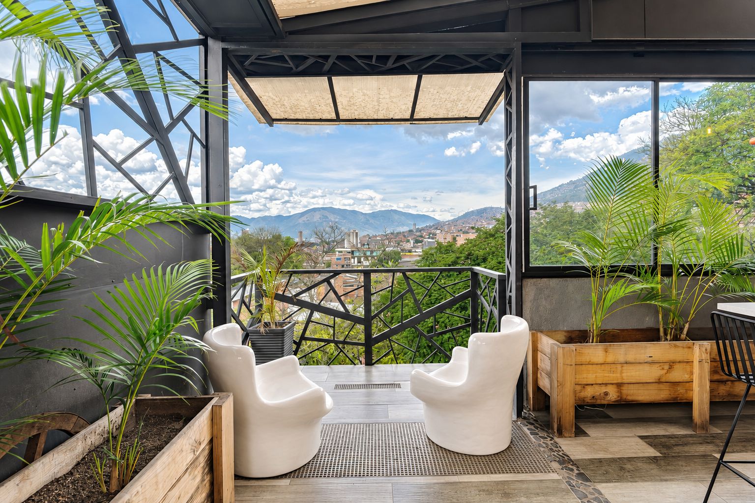 Un área de estar exterior moderna con sillas blancas y jardineras, con vistas a un paisaje urbano y montañas.