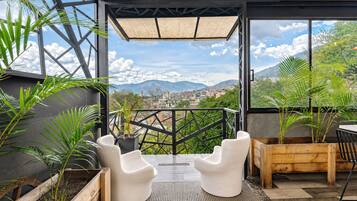Un área de estar exterior moderna con sillas blancas y jardineras, con vistas a un paisaje urbano y montañas.