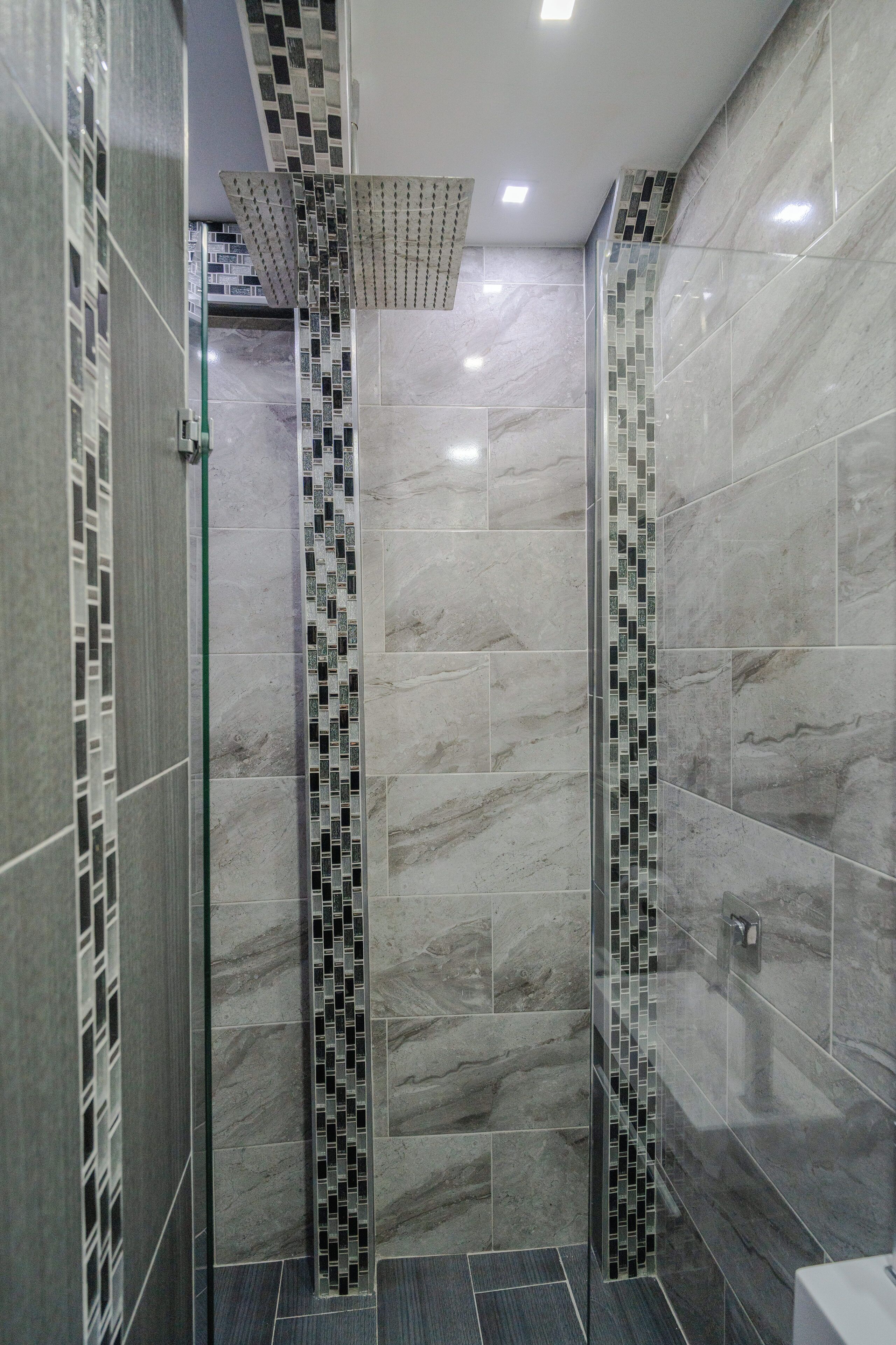 Un baño moderno con cabina de ducha de vidrio, paredes alicatadas y una franja decorativa de azulejos estampados.