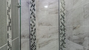 Une salle de bain moderne avec une douche à parois de verre, des murs carrelés et une bande décorative en carreaux à motifs.