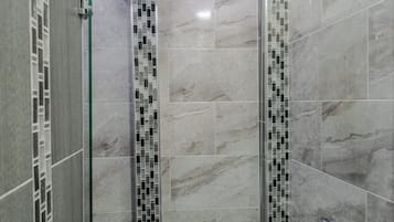 Un baño moderno con cabina de ducha de vidrio, paredes alicatadas y una franja decorativa de azulejos estampados.