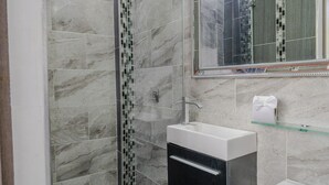 Une salle de bain moderne avec une douche à parois de verre, un lavabo blanc et un grand miroir au-dessus du lavabo.