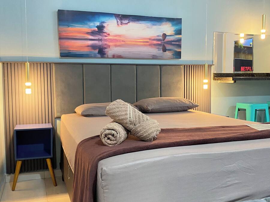 A modern bedroom with a large bed, a headboard, a side table, and a wall-mounted TV.
