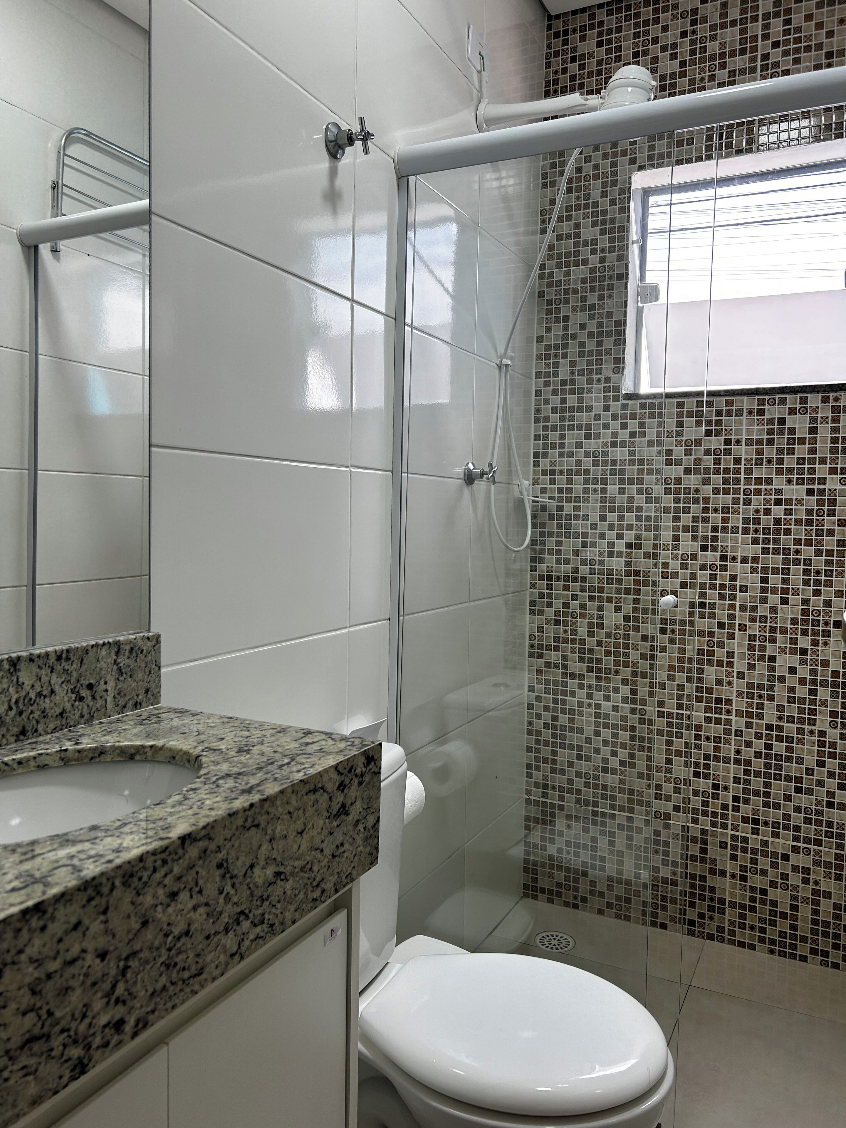 Une salle de bain dotée d’un plan de toilette en granit, de toilettes blanches, d’une cabine de douche et d’un mur carrelé orné d’un motif en mosaïque.