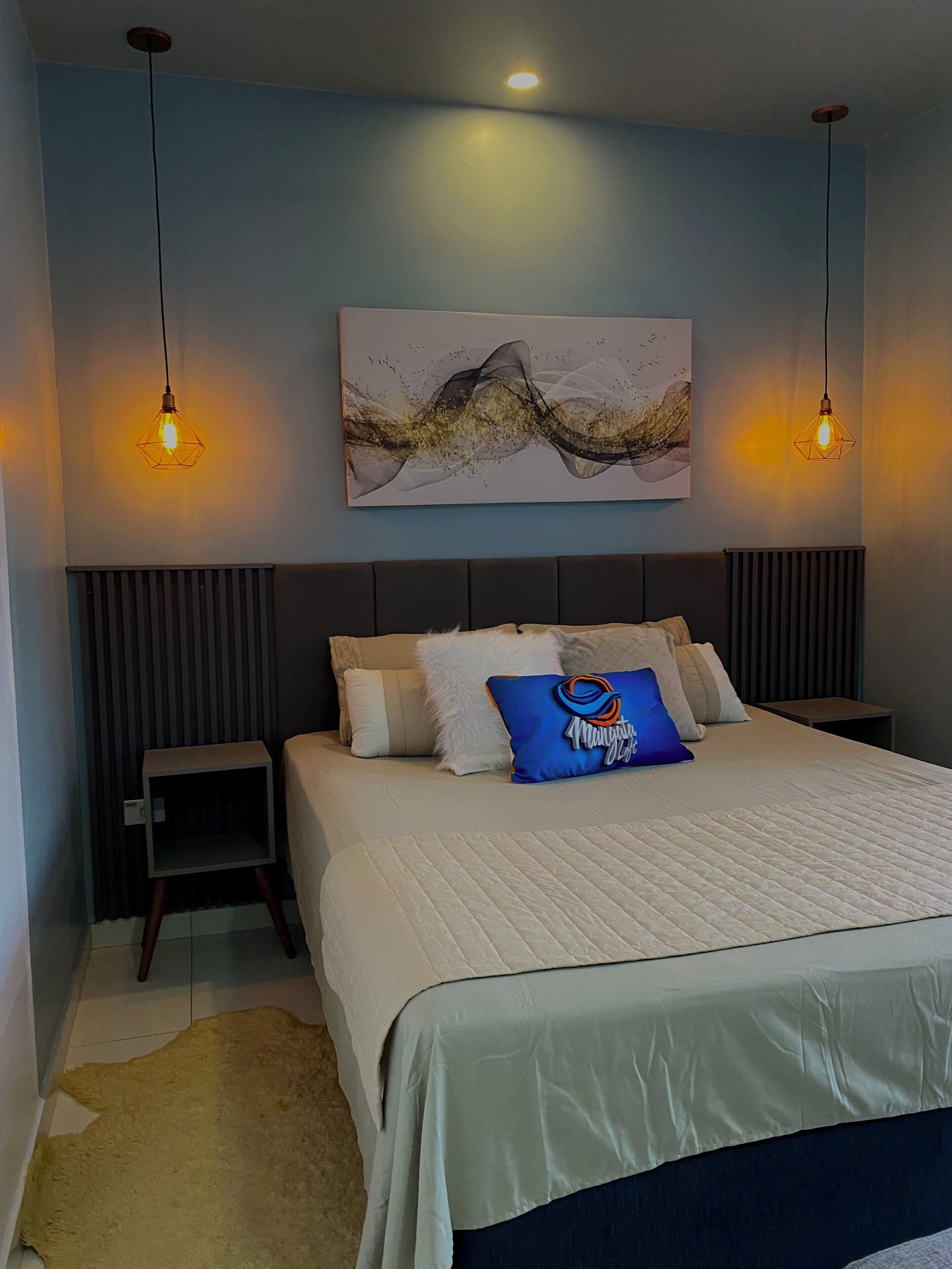 A modern bedroom with a bed, bedside tables, a rug, and a wall-mounted abstract painting.