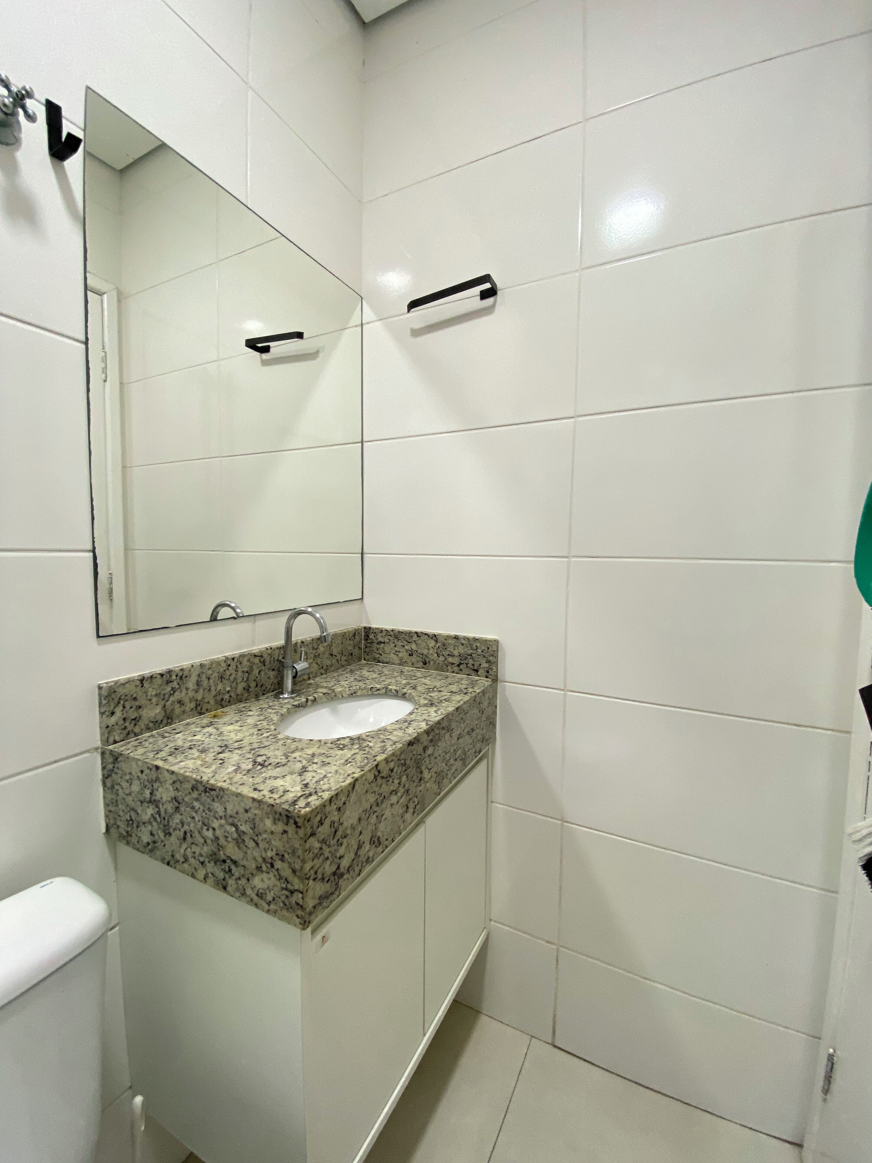 A bathroom with white tiled walls, a granite countertop sink, a mirror, and a towel rack.