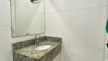 A bathroom with white tiled walls, a granite countertop sink, a mirror, and a towel rack.