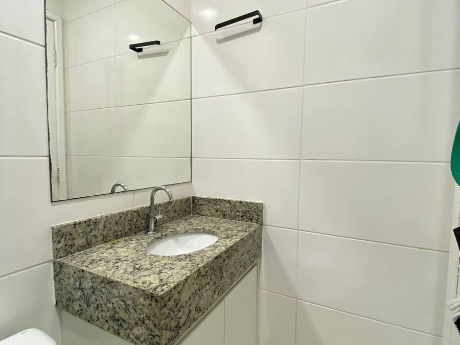 A bathroom with white tiled walls, a granite countertop sink, a mirror, and a towel rack.