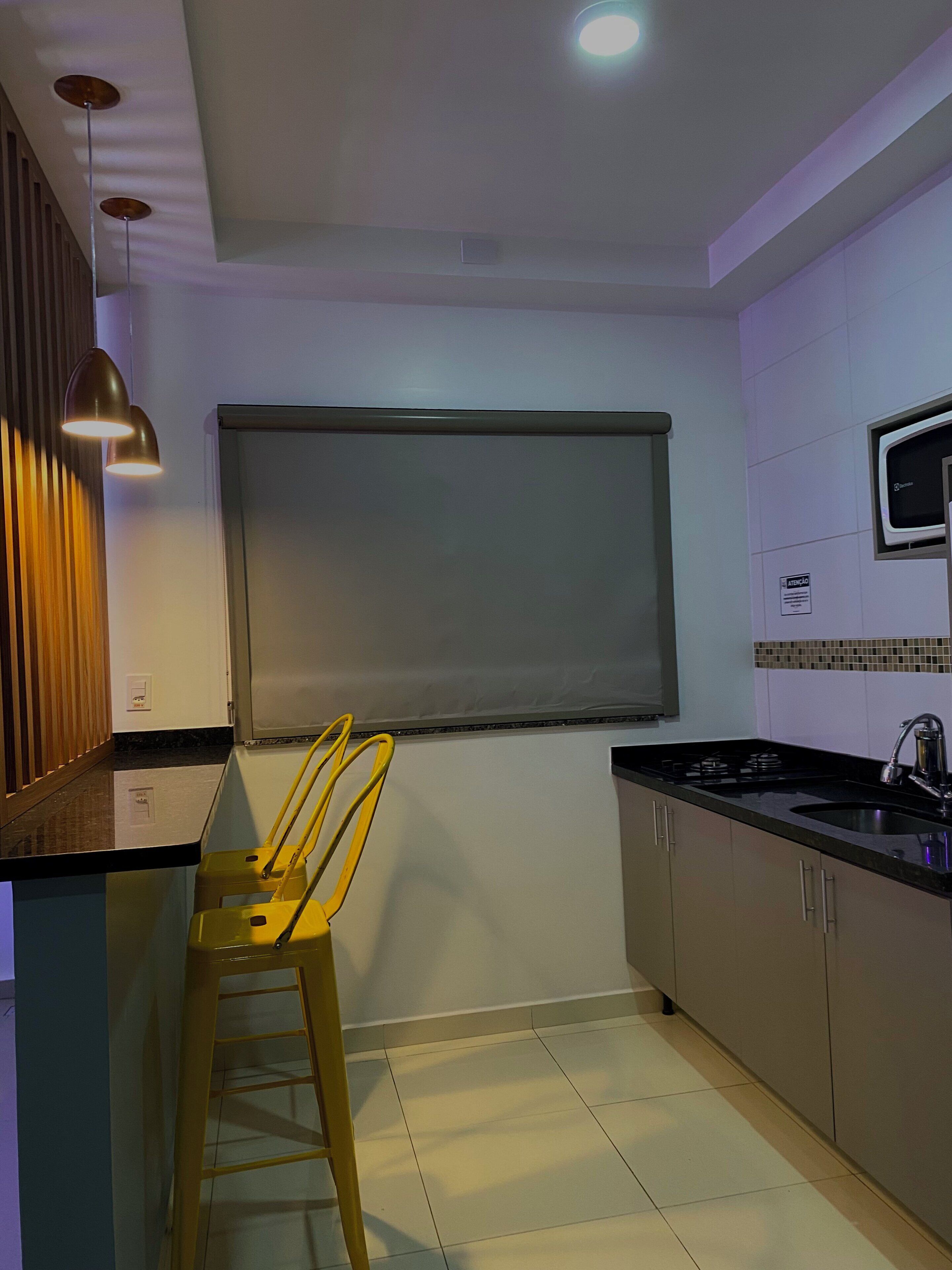 Une cuisine moderne avec un plan de travail noir, des appareils en acier inoxydable et un tabouret en bois.