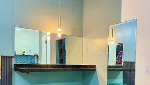 A bathroom with a large mirror, two turquoise stools, a blue cabinet, and a light fixture. - Mangata Loft (Itanhaém)