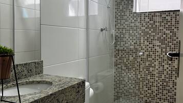 A bathroom with a white toilet, a granite countertop, a shower with a glass door, and a tiled backsplash.