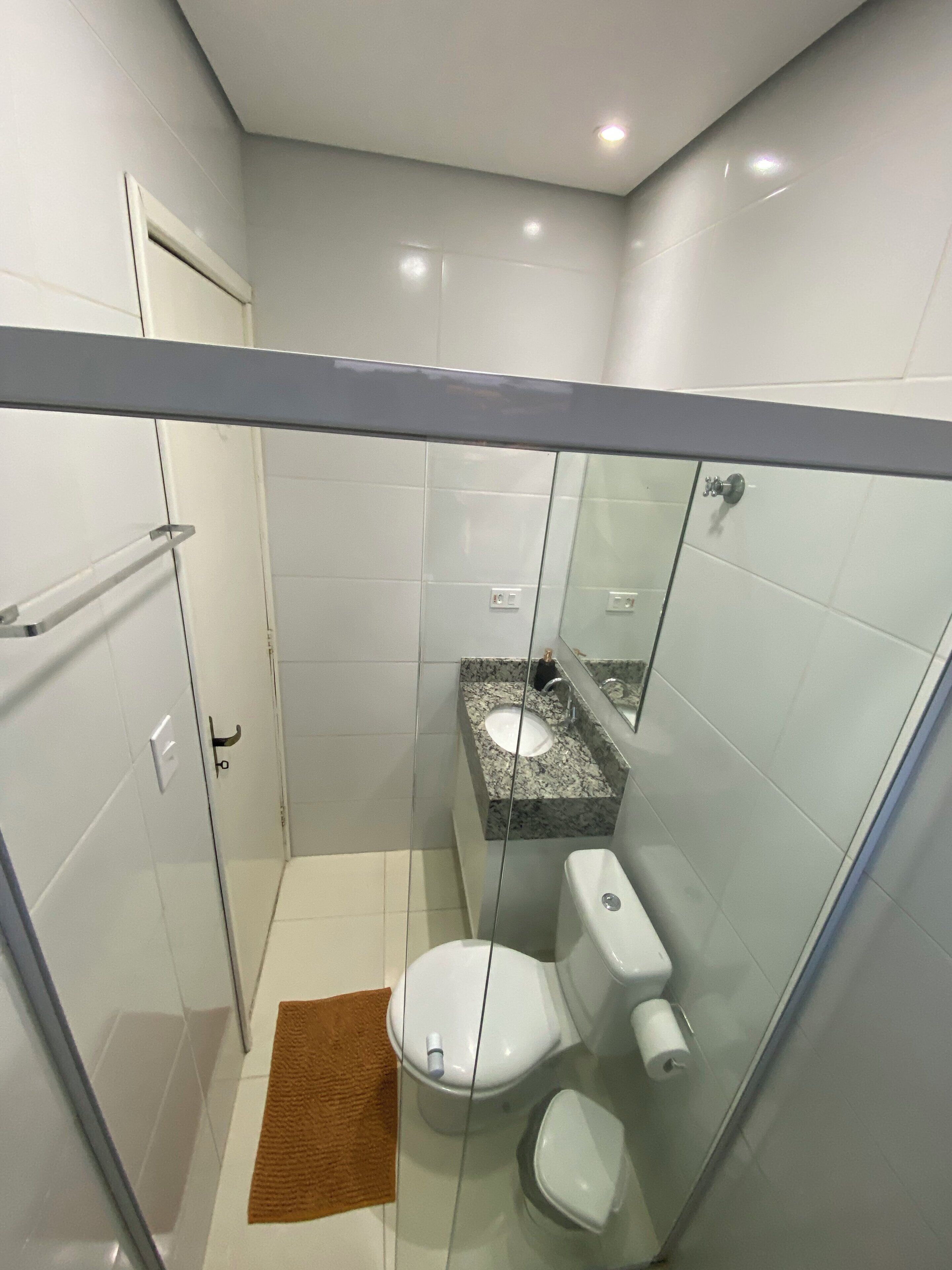 A small, modern bathroom with a glass shower enclosure, a toilet, and a sink with a granite countertop.