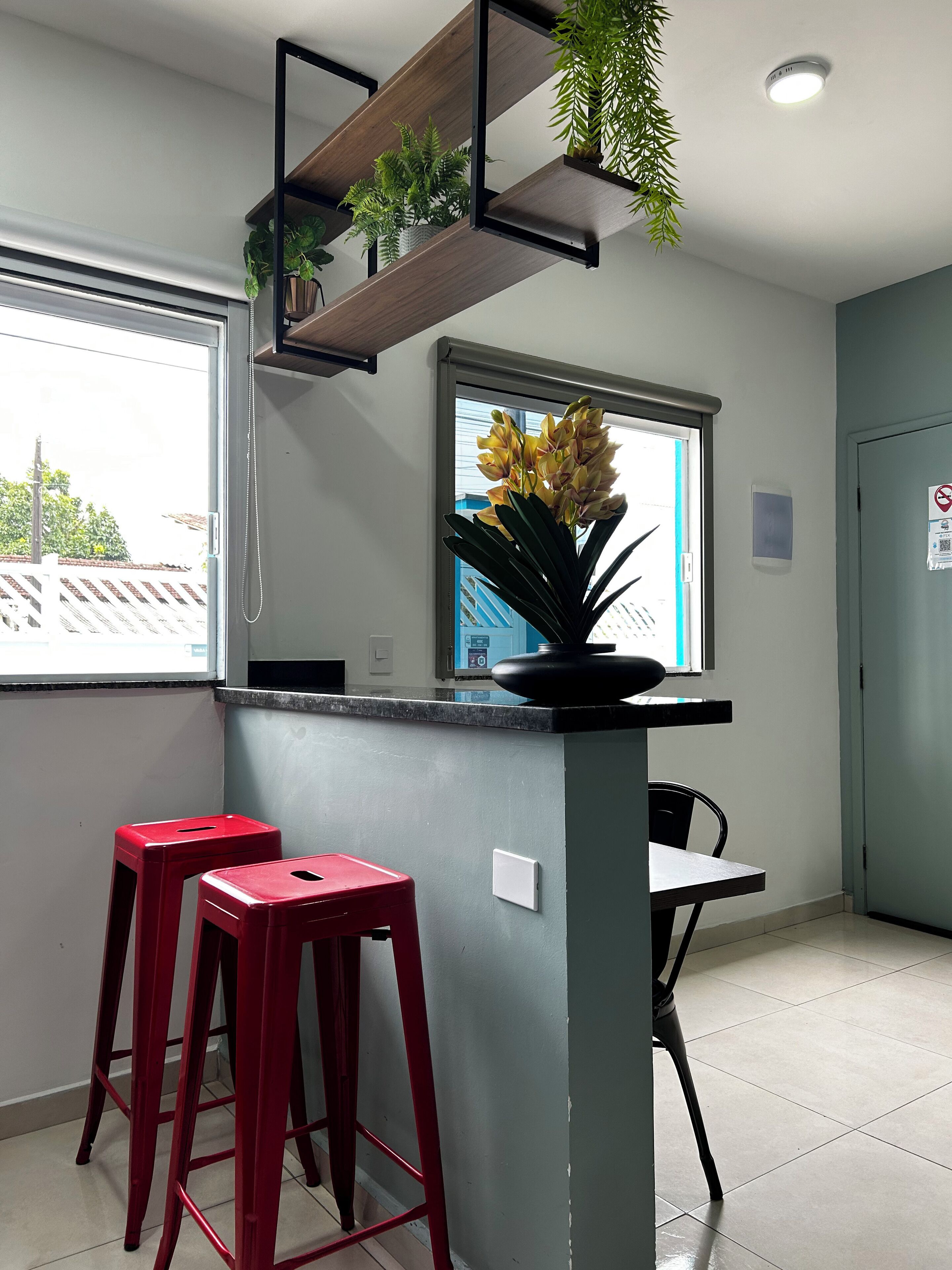A kitchen area with a window, a plant on a shelf, two red stools, and a table.